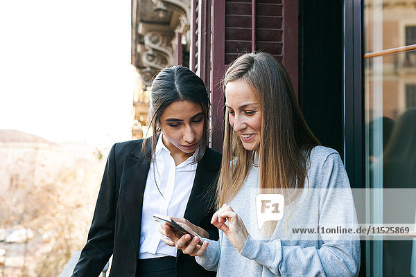 Two young women on balcony looking at cell phone