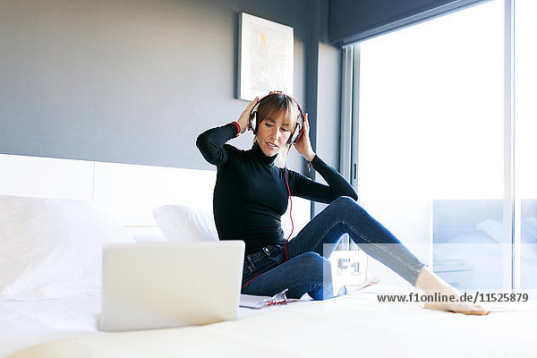 Junge Frau im Bett mit Laptop und Kopfhörer