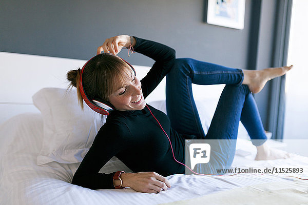 Happy young woman lying on bed wearing headphones