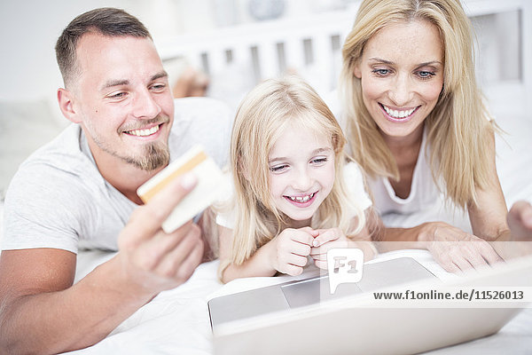 Smiling girl with parents lying in bed using laptop