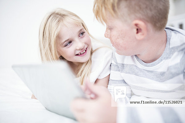 Brother and sister lying in bed using tablet