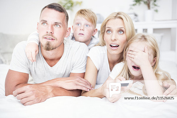 Happy family lying in bed watching Tv