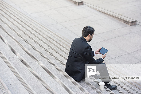 Geschäftsmann auf der Treppe sitzend mit Tablette und Kaffee zum Mitnehmen