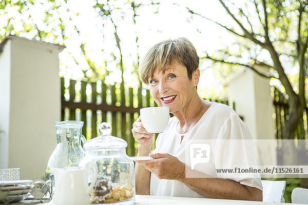 Porträt einer lächelnden Seniorin beim Kaffeetrinken im Freien
