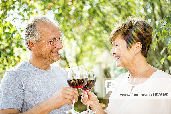 Lächelndes älteres Paar klirrende Rotweingläser im Freien