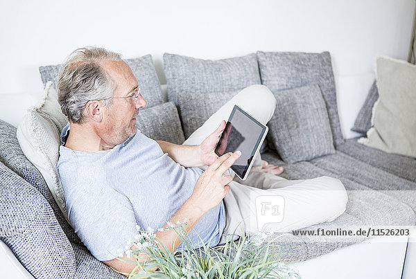 Mature man at home lying on couch using digital tablet