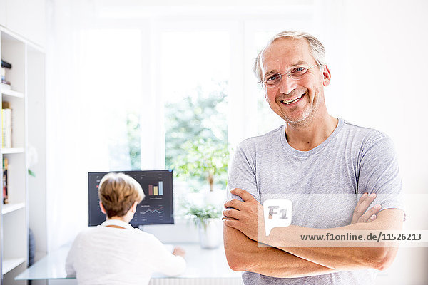 Portrait of smiling senior man with wife in background using computer