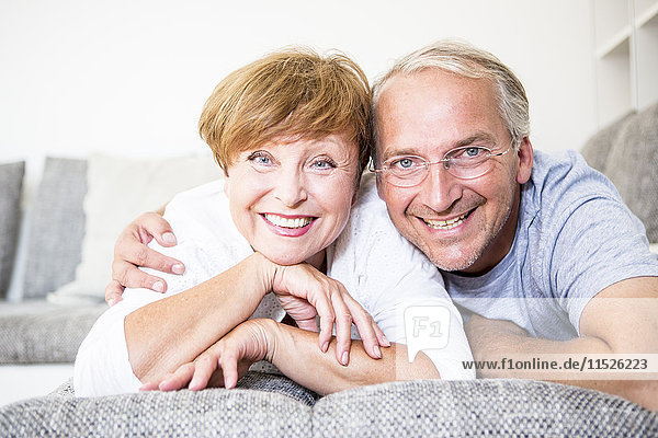 Portrait of smiling senior couple at home lying on couch