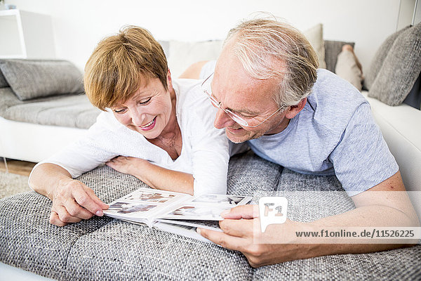 Senior couple at home lying on couch looking at photo album