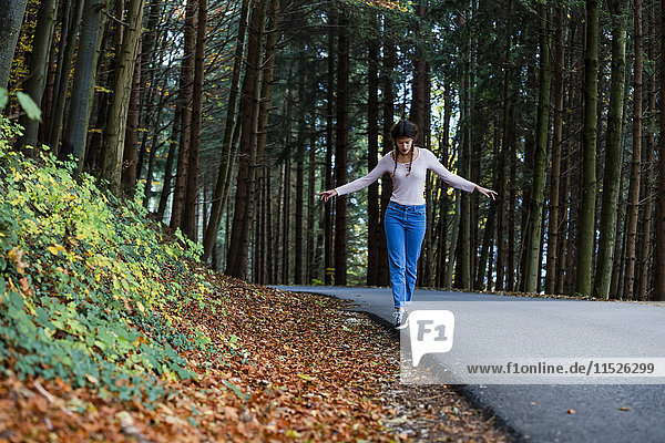 Junge Frau beim Balancieren am Straßenrand im Wald