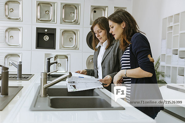 Customers consulting saleswoman in shop for kitchen sinks