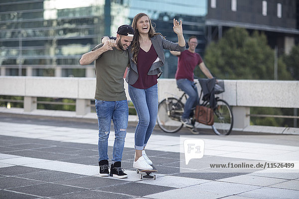 Young man supporting laughing girlfriend on skateboard