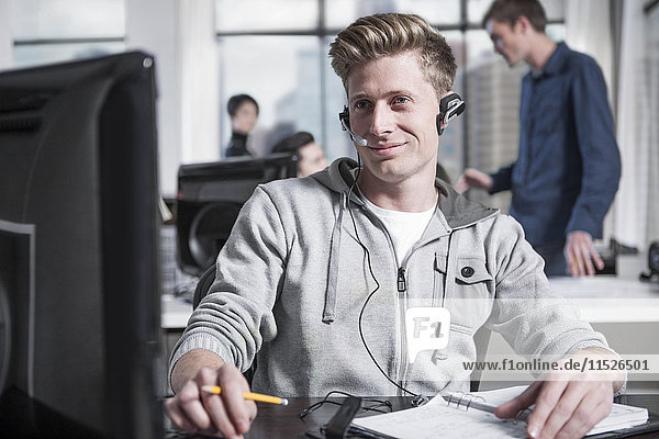 Junger Mann am Schreibtisch im Büro mit Headset