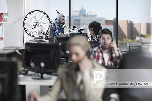 Lässiger Mann mit Fahrrad im modernen Büro im Gespräch mit einer Kollegin