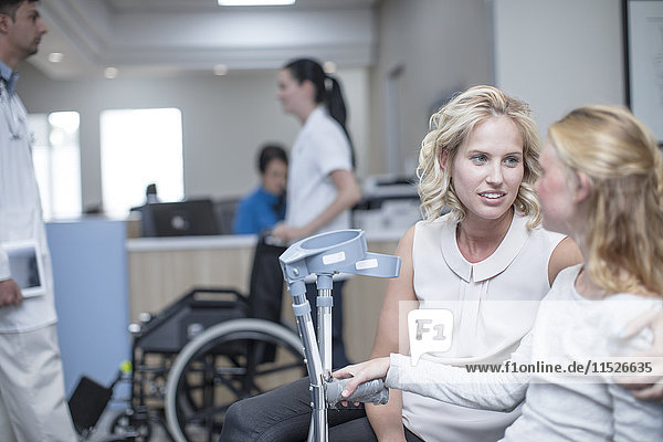Girl with crutches sitting with her mother in reception area