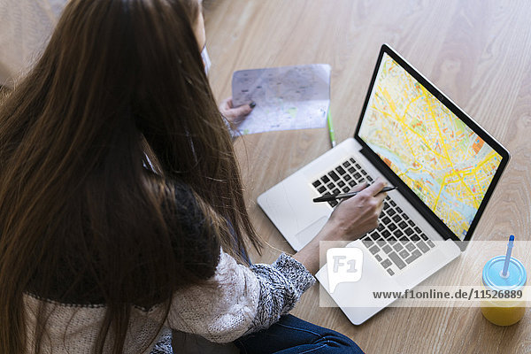 Junge Frau auf dem Boden sitzend mit Blick auf die Karte auf dem Laptop