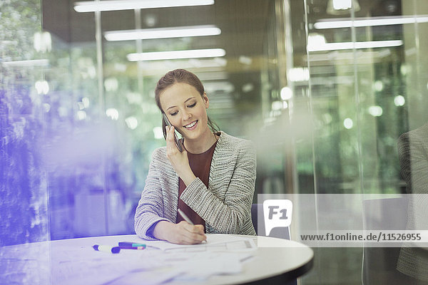 Lächelnde Geschäftsfrau beim Telefonieren und Notieren im Konferenzraum