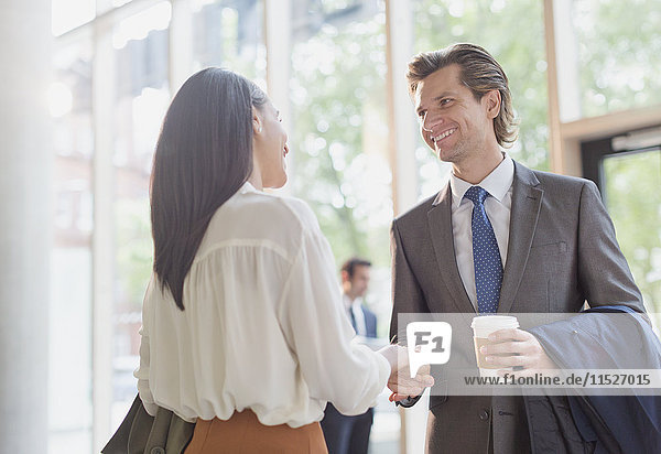 Businessman with coffee and businesswoman handshaking in office lobby