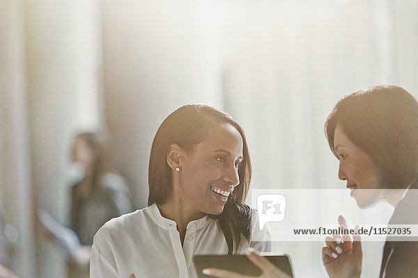Lächelnde Geschäftsfrauen beim Sprechen mit dem digitalen Tablett