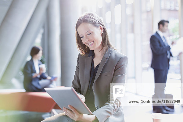 Smiling businesswoman using digital tablet in sunny office lobby