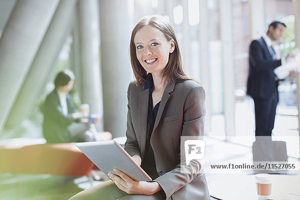 Portrait smiling businesswoman using digital tablet in sunny office lobby