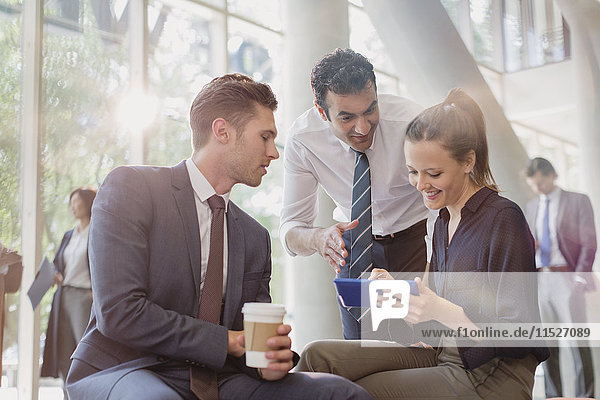 Business people with coffee using digital tablet  talking in office lobby