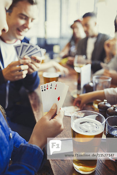 Frau hält Asse in der Hand  spielt Poker und trinkt Bier mit Freunden an der Bar.