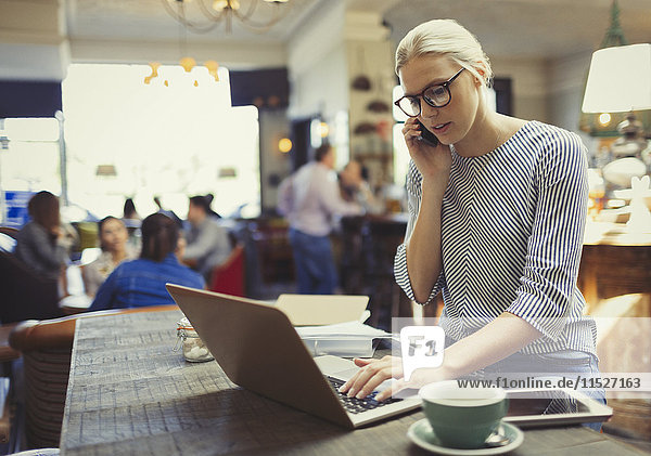 Kreative Geschäftsfrau spricht am Handy und nutzt Laptop im Cafe