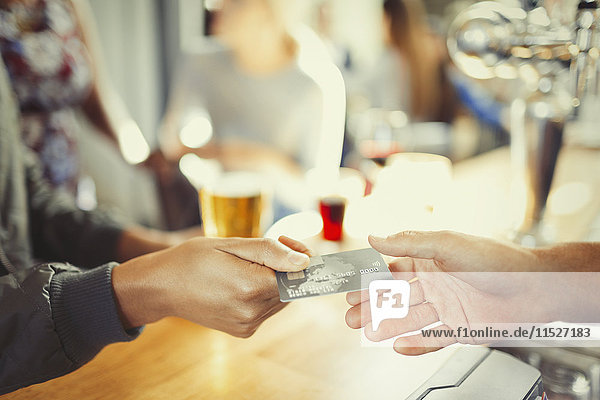 Frau bezahlt Barkeeperin mit Kreditkarte an der Bar