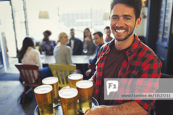 Portrait smiling bartender carrying tray of beer glasses in bar