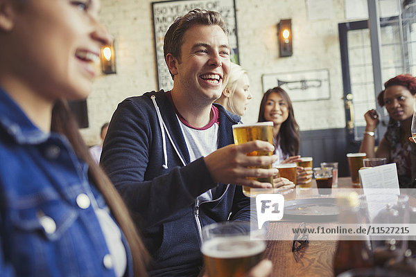 Smiling man drinking beer with friends at table in bar