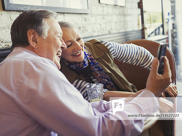 Lächelndes Seniorenpaar nimmt Selfie mit Fotohandy am Kaffeetisch mit.
