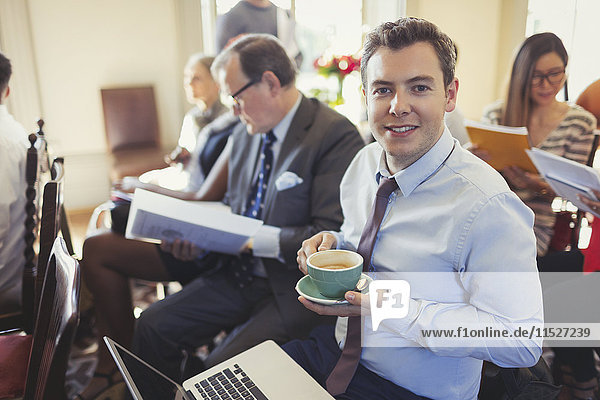 Portrait smiling businessman drinking coffee and using laptop in business conference audience