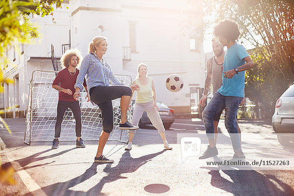 Freunde spielen Fußball in der sonnigen Sommerstraße