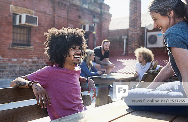 Lächelnde Freunde  die sich auf einem sonnigen  städtischen Dach unterhalten.
