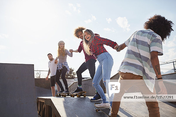 Freunde auf Skateboards halten Hand in Hand auf der Rampe im sonnigen Skatepark.