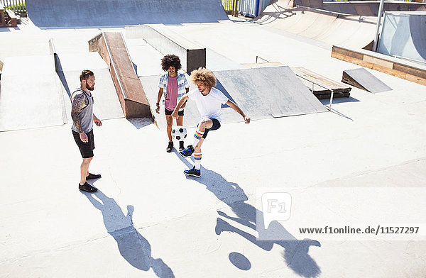 Männliche Freunde spielen Fußball im sonnigen Skatepark