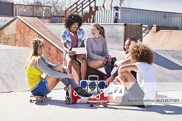 Freunde in Rollschuhen und auf dem Skateboard mit digitalem Tablett im sonnigen Skatepark