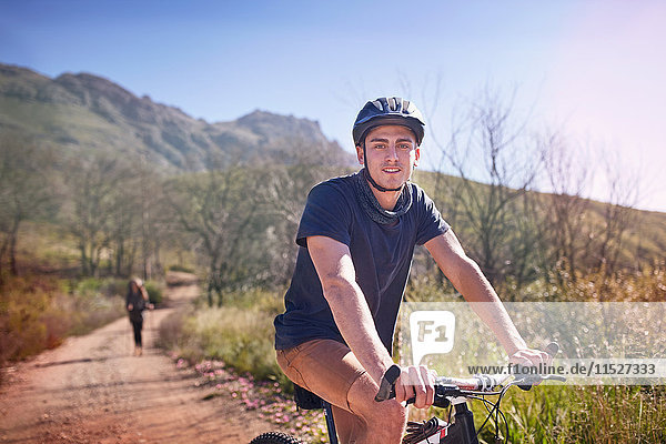 Portrait junger Mann Mountainbiken auf abgelegenem  sonnigem Weg