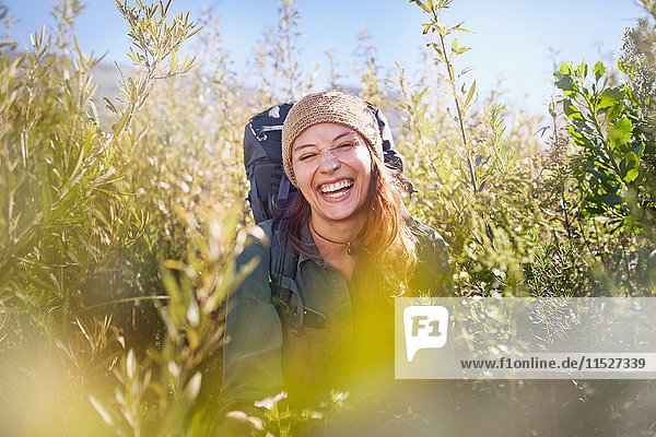 Portrait laughing young woman with backpack hiking in sunny field