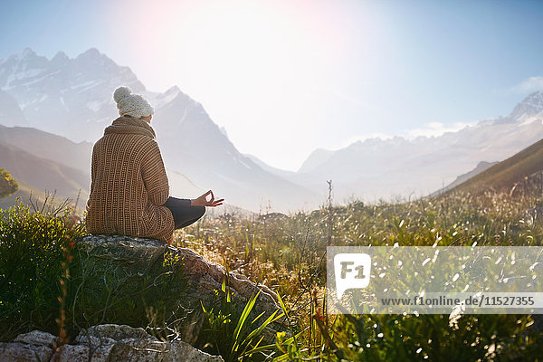 Young woman meditating on rock in sunny  remote valley