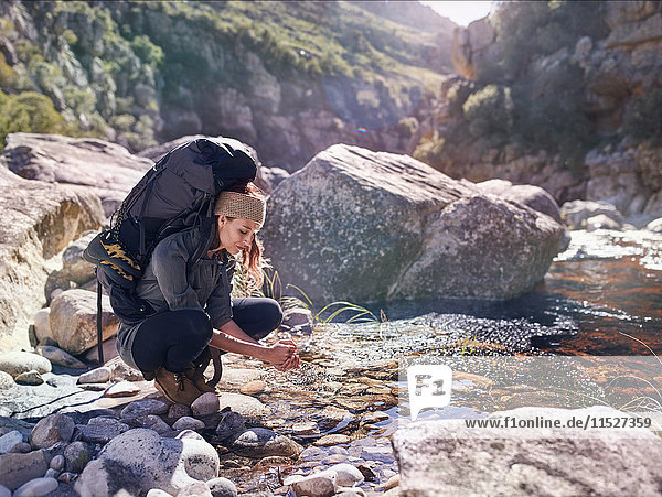 Young woman with backpack hiking  washing hands at sunny stream