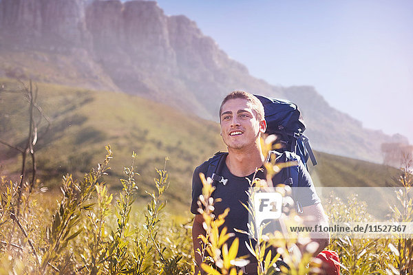Young man with backpack hiking in sunny valley
