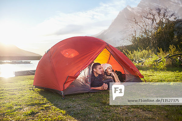 Young couple relaxing in tent at sunny lakeside campsite