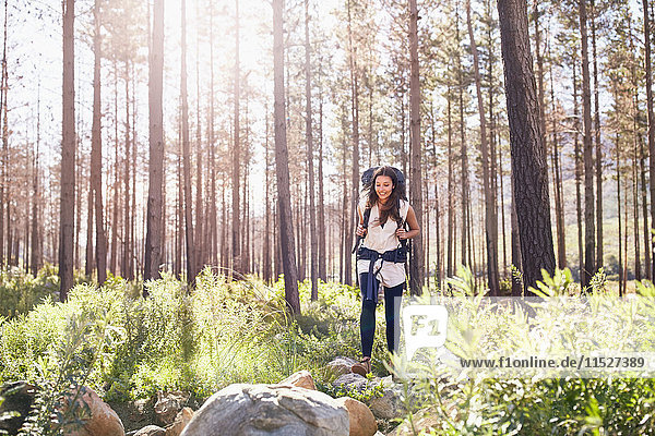 Smiling young woman with backpack hiking in sunny woods