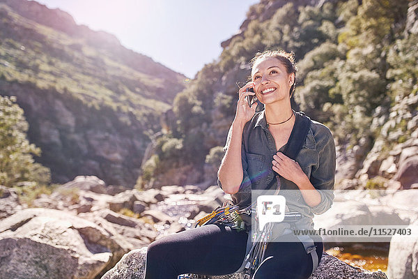 Young woman talking on cell phone below sunny  craggy cliffs