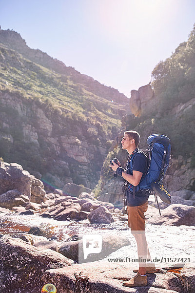Young man with backpack hiking and photographing sunny  craggy cliffs with camera