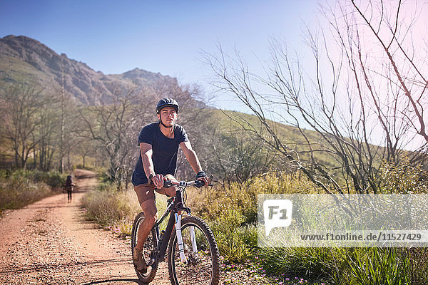 Young man mountain biking on sunny  remote dirt road