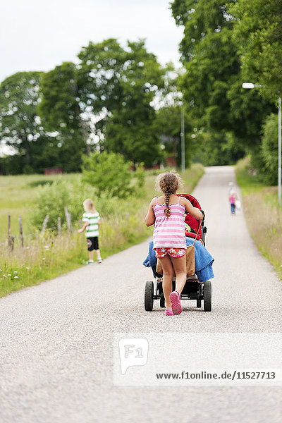 Mädchen schiebt Kinderwagen auf Landstraße