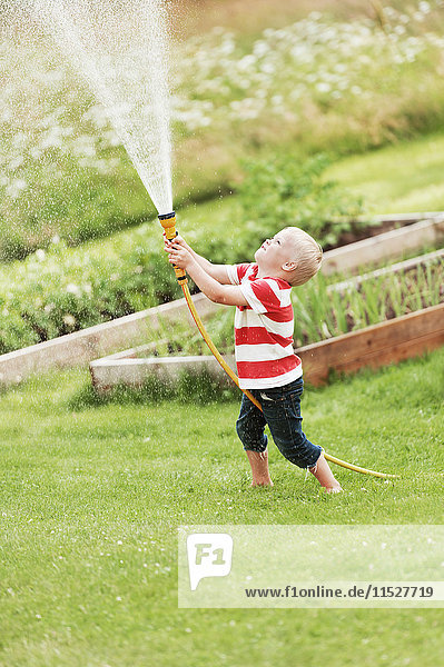 Junge spielt mit Gartenschlauch